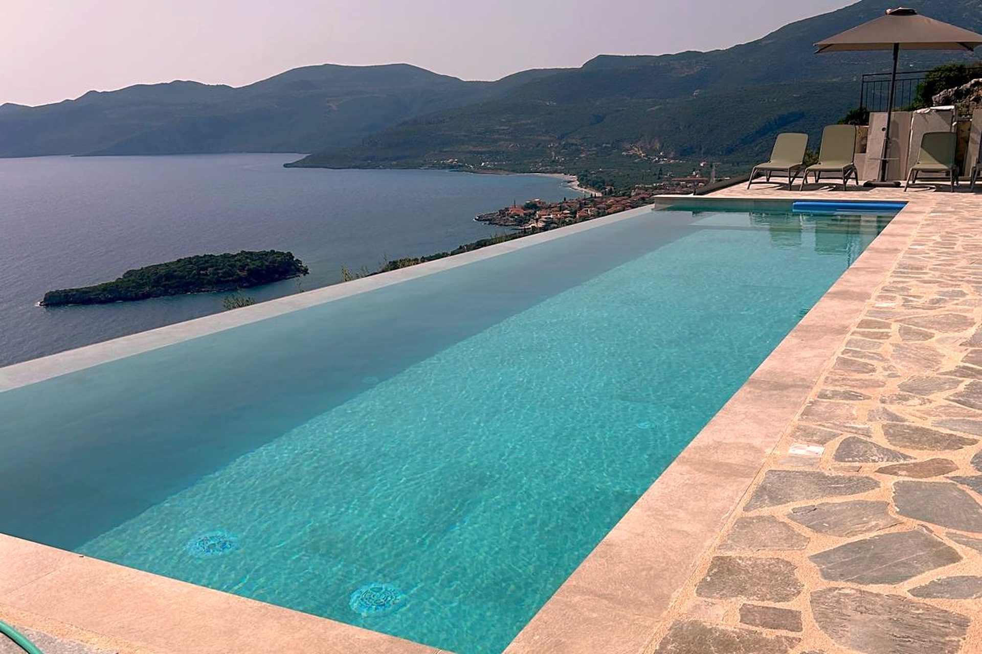 The full length of the infinity pool from the shallow end, the stone terrace around it and Kalamitsi bay below.